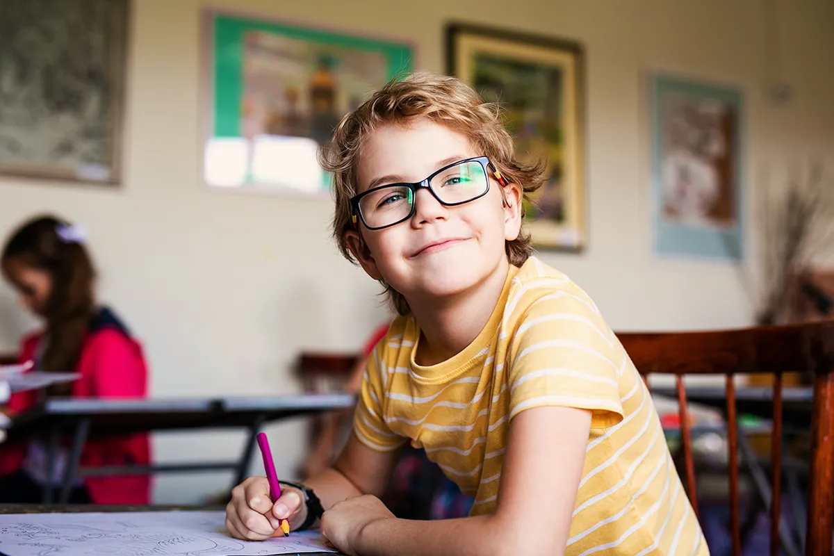 a little boy with glasses in a classroom smiling
